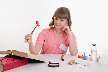 Image showing Medical student sitting at a table with tweezers on the pill