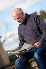 Image showing Man sitting reading a newspaper on a stone wall