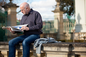 Image showing Man sitting reading a newspaper on a stone wall