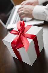 Image showing White Gift Box with Red Bow Near Man using Laptop