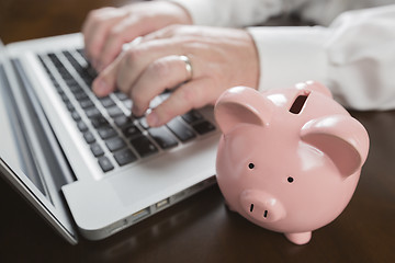 Image showing Piggy Bank Near Male Hands Typing on Laptop