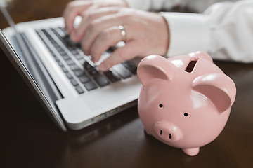 Image showing Piggy Bank Near Male Hands Typing on Laptop