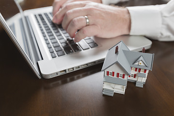 Image showing Miniature House Near Man Typing on Laptop Computer