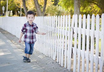 Image showing Young Mixed Race Boy Walking with Stick Along White Fence