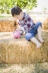 Image showing Cute Young Mixed Race Boy Putting Coins Into Piggy Bank