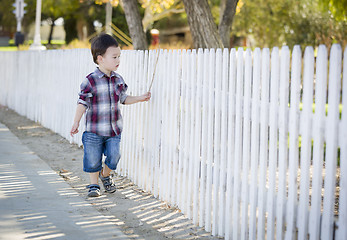 Image showing Young Mixed Race Boy Walking with Stick Along White Fence