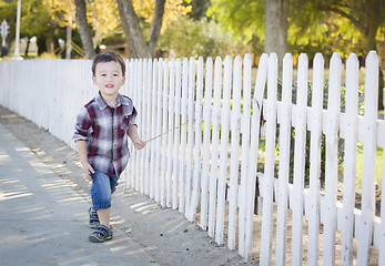 Image showing Young Mixed Race Boy Walking with Stick Along White Fence