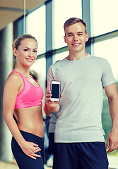 Image showing smiling young woman with personal trainer in gym