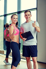 Image showing smiling young woman with personal trainer in gym