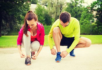 Image showing smiling couple tying shoelaces outdoors