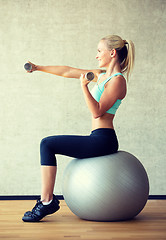 Image showing smiling woman with dumbbells and exercise ball