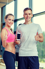 Image showing smiling young woman with personal trainer in gym