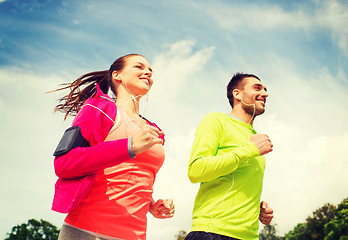 Image showing smiling couple with earphones running outdoors