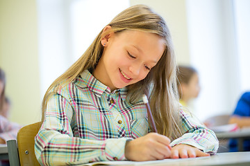 Image showing smiling school girl writing test in classroom