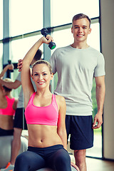 Image showing smiling young woman with personal trainer in gym