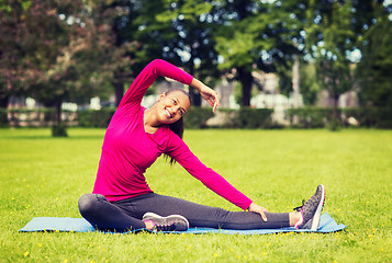 Image showing smiling woman stretching leg on mat outdoors