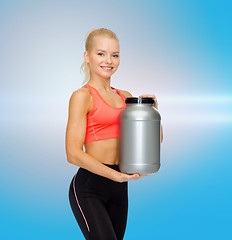 Image showing smiling sporty woman with jar of protein