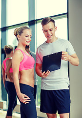 Image showing smiling young woman with personal trainer in gym