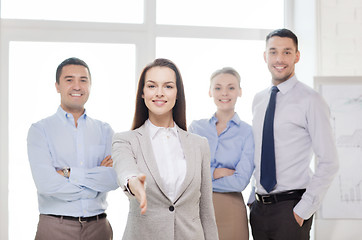 Image showing smiling businesswoman in office with team on back