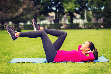 Image showing smiling woman doing exercises on mat outdoors