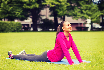 Image showing smiling woman stretching on mat outdoors