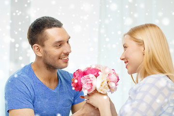 Image showing smiling man giving girlfriend flowers at home