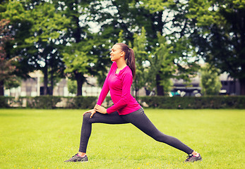 Image showing smiling black woman stretching leg outdoors