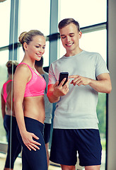 Image showing smiling young woman with personal trainer in gym