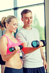 Image showing smiling young woman with personal trainer in gym