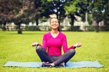 Image showing smiling woman meditating on mat outdoors