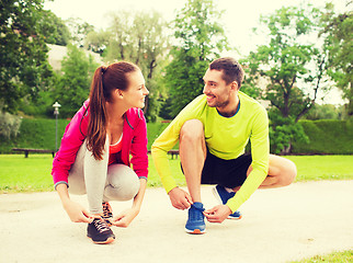 Image showing smiling couple tying shoelaces outdoors