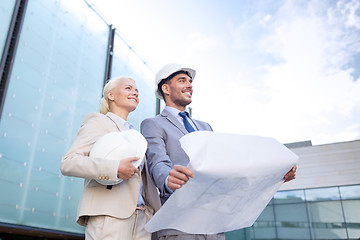 Image showing smiling businessmen with blueprint and helmets