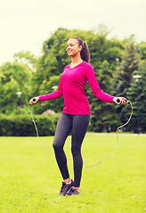 Image showing smiling woman exercising with jump-rope outdoors