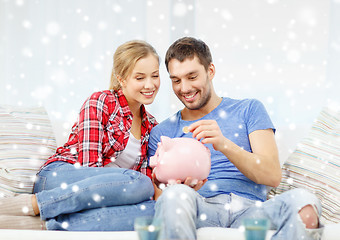 Image showing smiling couple with piggybank sitting on sofa