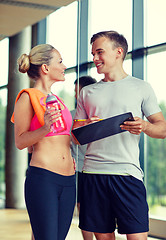 Image showing smiling young woman with personal trainer in gym