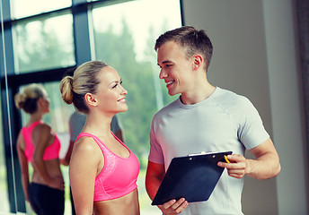 Image showing smiling young woman with personal trainer in gym