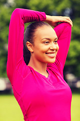 Image showing smiling black woman stretching leg outdoors