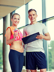 Image showing smiling young woman with personal trainer in gym