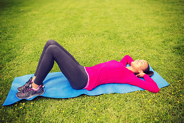 Image showing smiling woman doing exercises on mat outdoors
