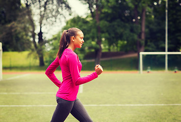 Image showing smiling young woman running on track outdoors