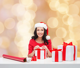 Image showing smiling woman in santa helper hat packing gifts