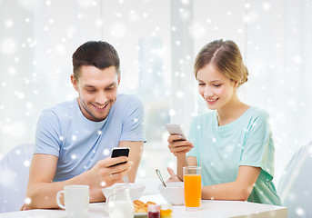 Image showing smiling couple with smartphones having breakfast