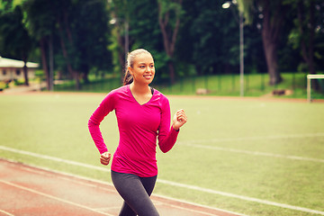 Image showing smiling woman running on track outdoors