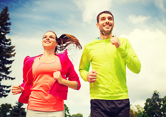 Image showing smiling couple with earphones running outdoors