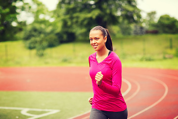 Image showing smiling young woman running on track outdoors