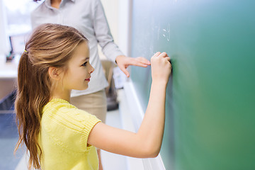 Image showing little smiling schoolgirl writing on chalk board