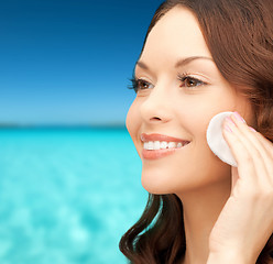 Image showing smiling woman cleaning face skin with cotton pad