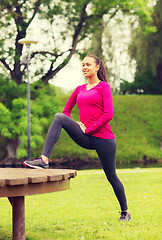 Image showing smiling woman stretching on bench outdoors