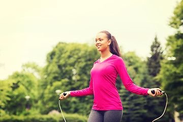 Image showing smiling woman exercising with jump-rope outdoors