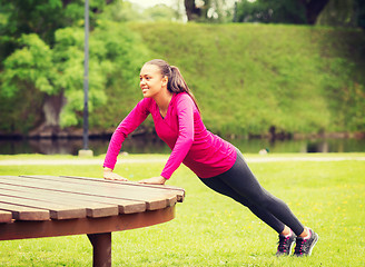 Image showing smiling woman doing push-ups on bench outdoors